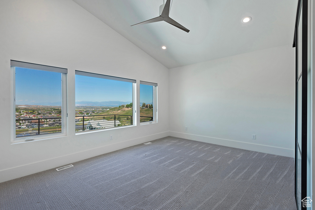 Empty room with dark carpet, ceiling fan, and a wealth of natural light