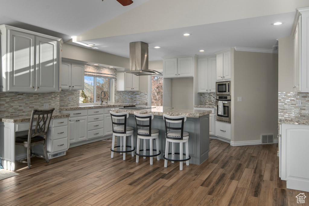 Kitchen featuring a kitchen breakfast bar, ceiling fan, appliances with stainless steel finishes, white cabinets, and island range hood