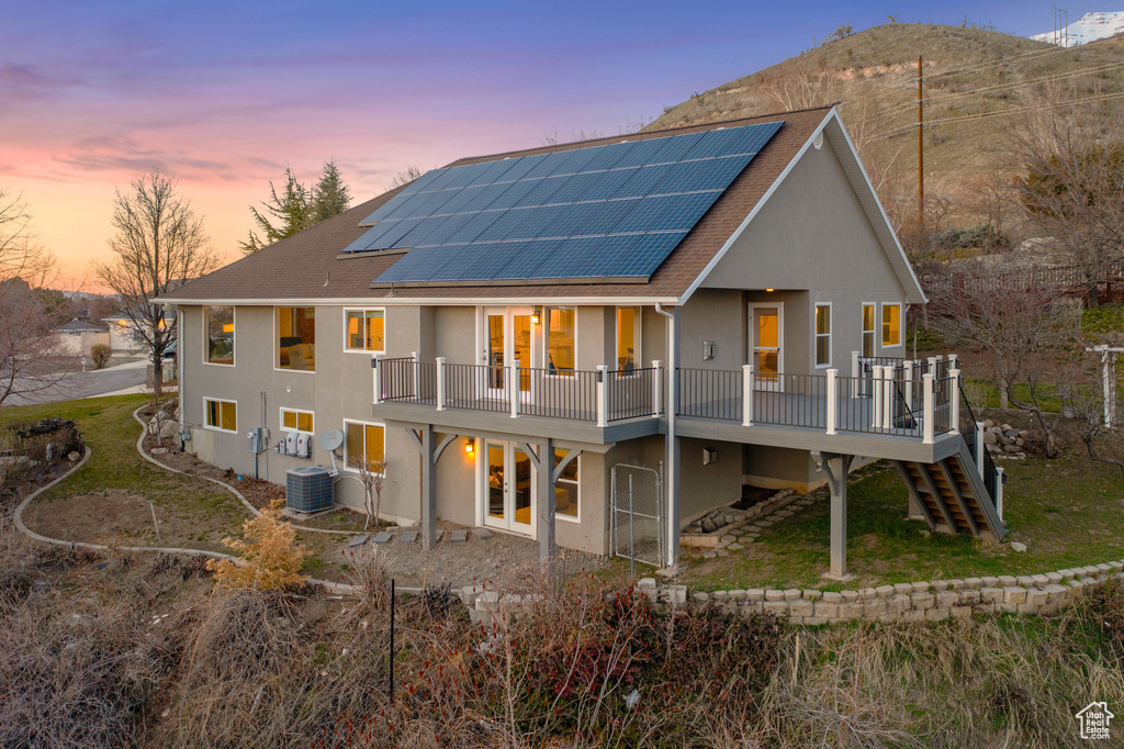 Back house at dusk with a balcony, central AC unit, and solar panels