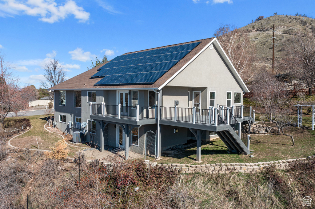 Back of property with central AC, a lawn, a wooden deck, and solar panels