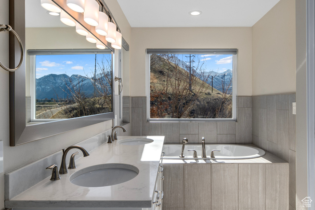 Bathroom featuring a relaxing tiled bath, double sink, vanity with extensive cabinet space, and a mountain view