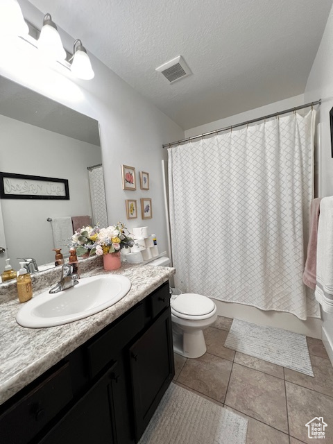 Bathroom featuring large vanity, a textured ceiling, toilet, and tile flooring