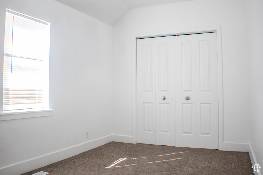 Unfurnished bedroom featuring dark colored carpet, lofted ceiling, and a closet