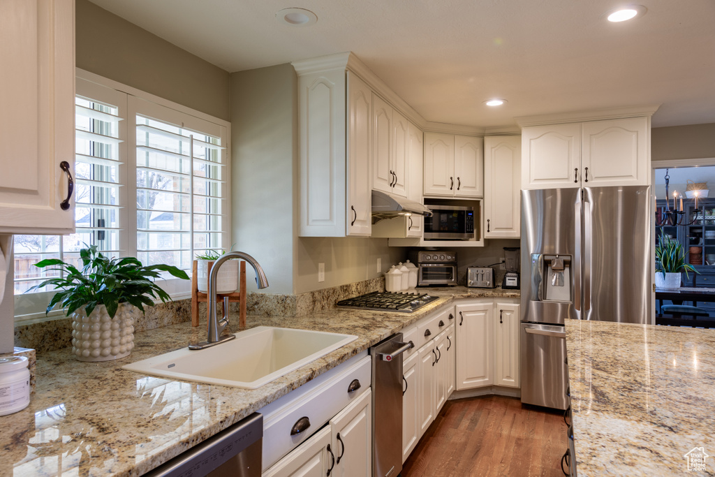 Kitchen featuring white cabinets, hardwood / wood-style floors, stainless steel appliances, sink, and light stone countertops