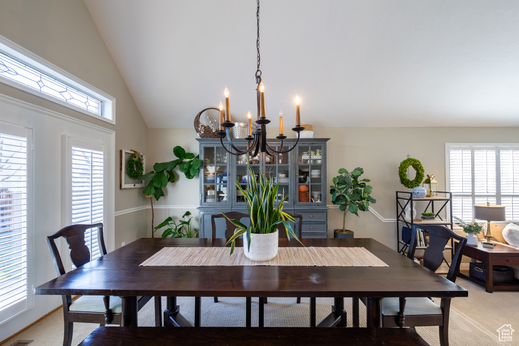 Carpeted dining room with a chandelier, high vaulted ceiling, and a healthy amount of sunlight