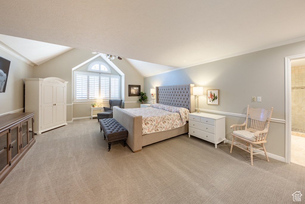 Bedroom with light colored carpet, crown molding, vaulted ceiling, and connected bathroom