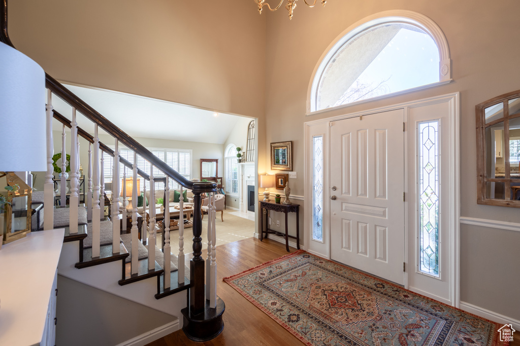 Foyer entrance with plenty of natural light, an inviting chandelier, light wood-type flooring, and high vaulted ceiling