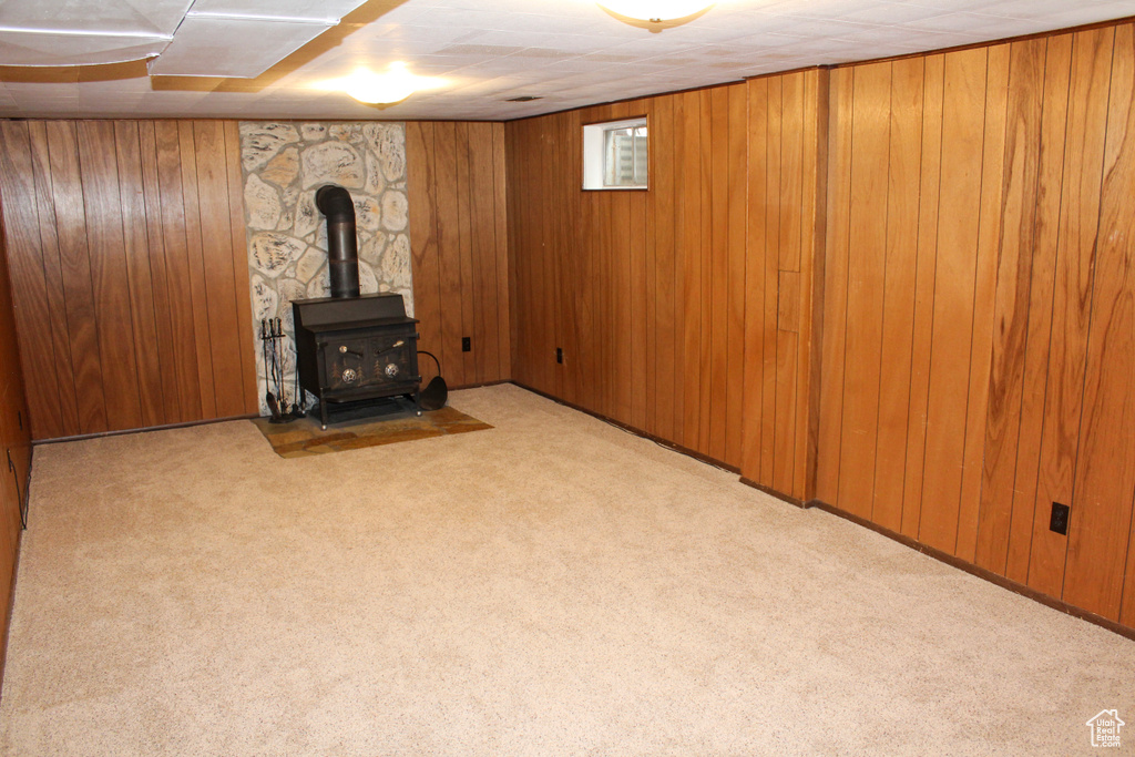 Basement featuring wood walls, light carpet, and a wood stove