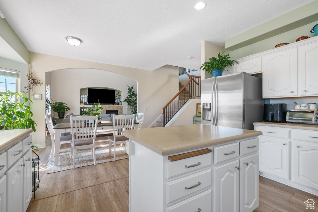Kitchen with white cabinets, stainless steel fridge with ice dispenser, a center island, and light hardwood / wood-style flooring