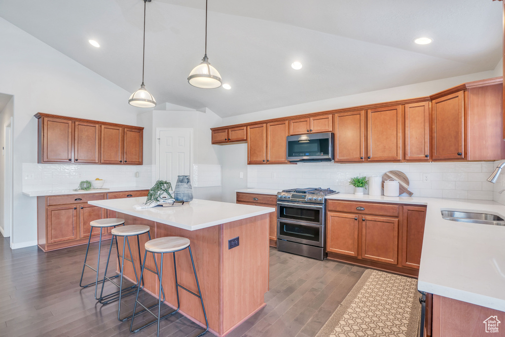 Kitchen with stainless steel appliances, dark hardwood / wood-style flooring, hanging light fixtures, a kitchen island, and tasteful backsplash