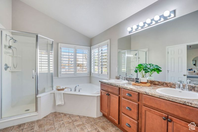 Bathroom with tile floors, dual bowl vanity, vaulted ceiling, and independent shower and bath