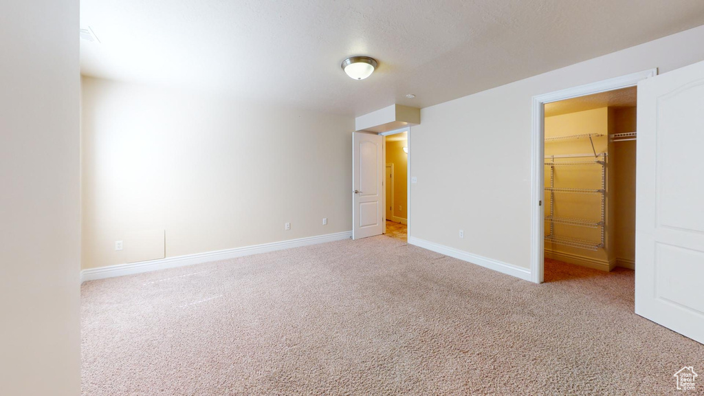 Unfurnished bedroom with light colored carpet, a walk in closet, and a closet