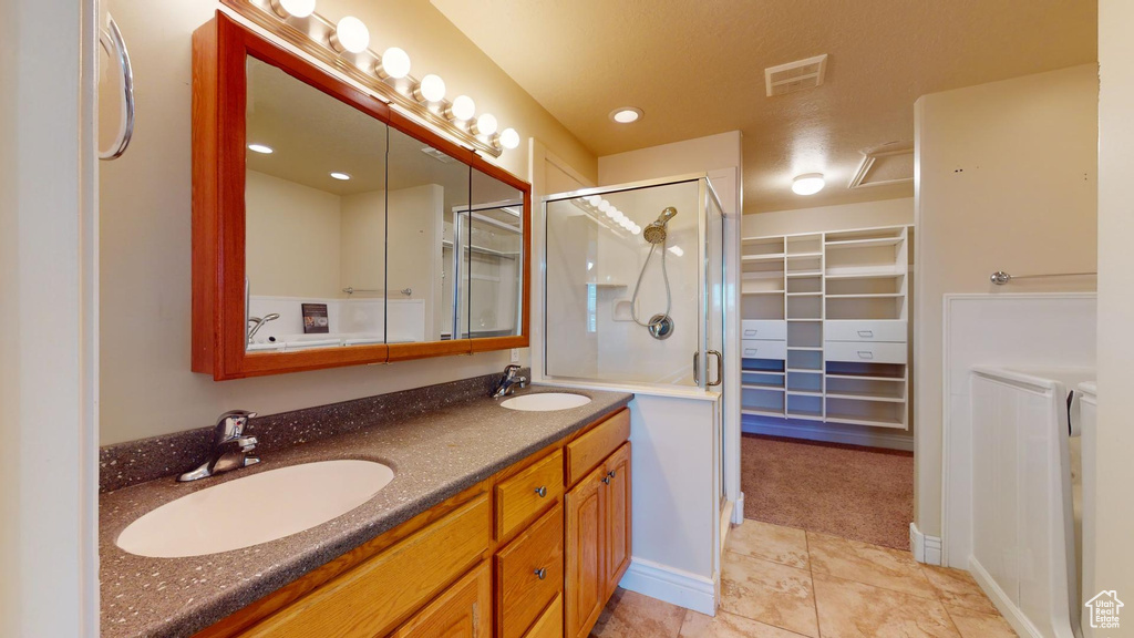 Bathroom featuring double sink, walk in shower, tile flooring, washer and clothes dryer, and vanity with extensive cabinet space