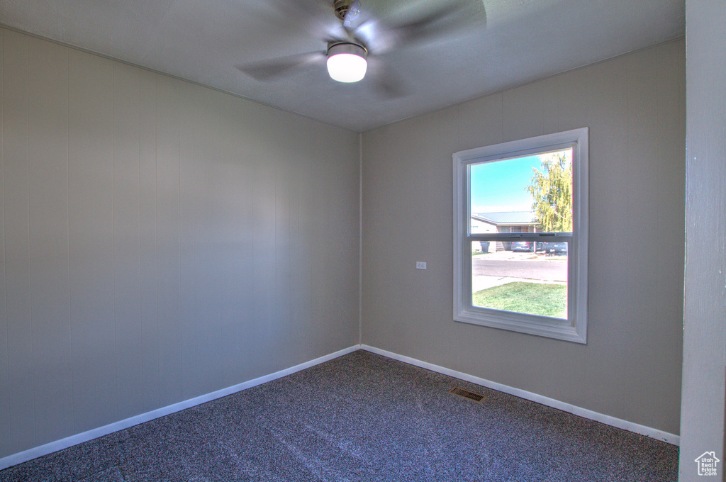 Spare room with dark carpet, a wealth of natural light, and ceiling fan