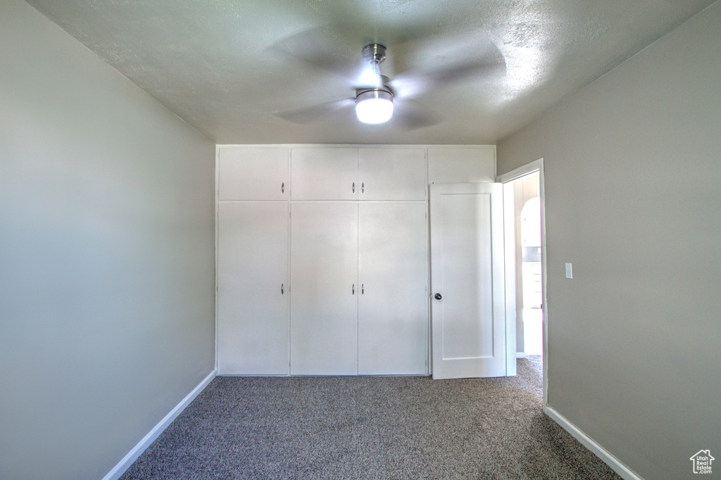 Unfurnished bedroom featuring a closet, ceiling fan, and dark colored carpet