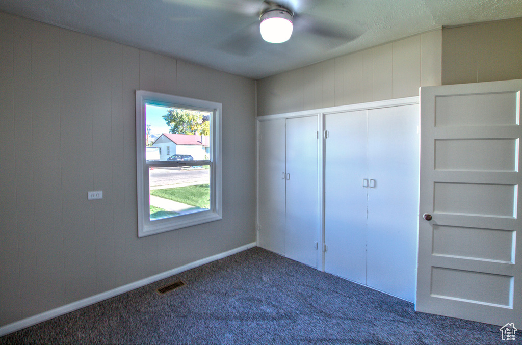 Unfurnished bedroom featuring multiple windows, dark colored carpet, a closet, and ceiling fan