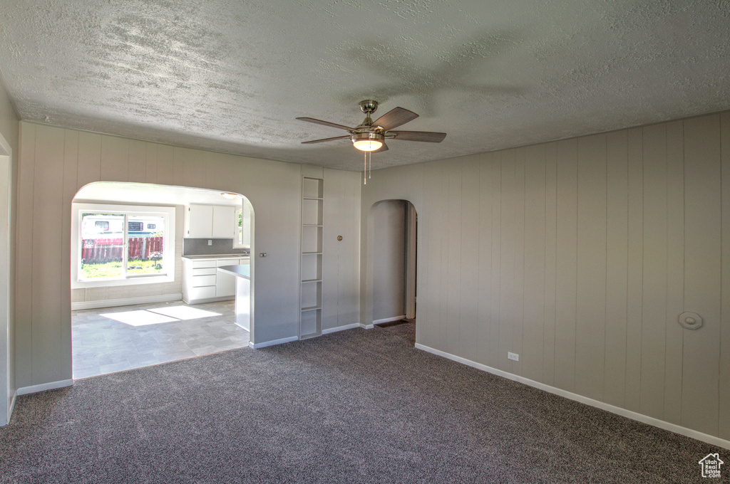 Unfurnished room featuring a textured ceiling, ceiling fan, and dark colored carpet