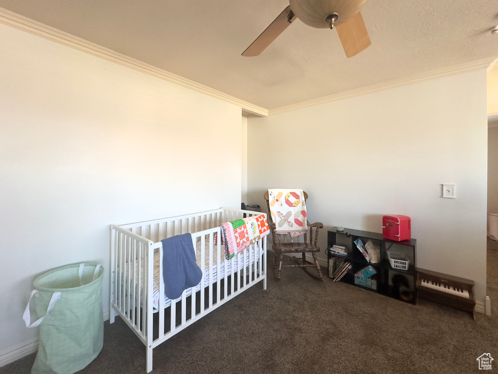 Carpeted bedroom with crown molding, a nursery area, and ceiling fan