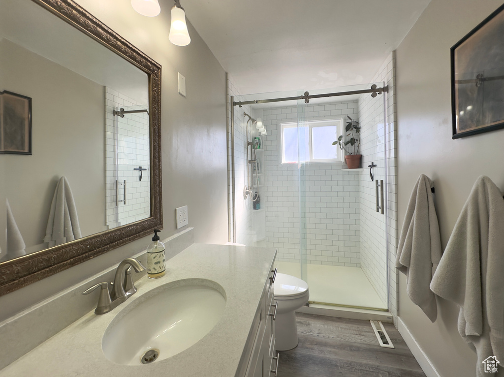 Bathroom with a shower with door, vanity with extensive cabinet space, hardwood / wood-style flooring, and toilet
