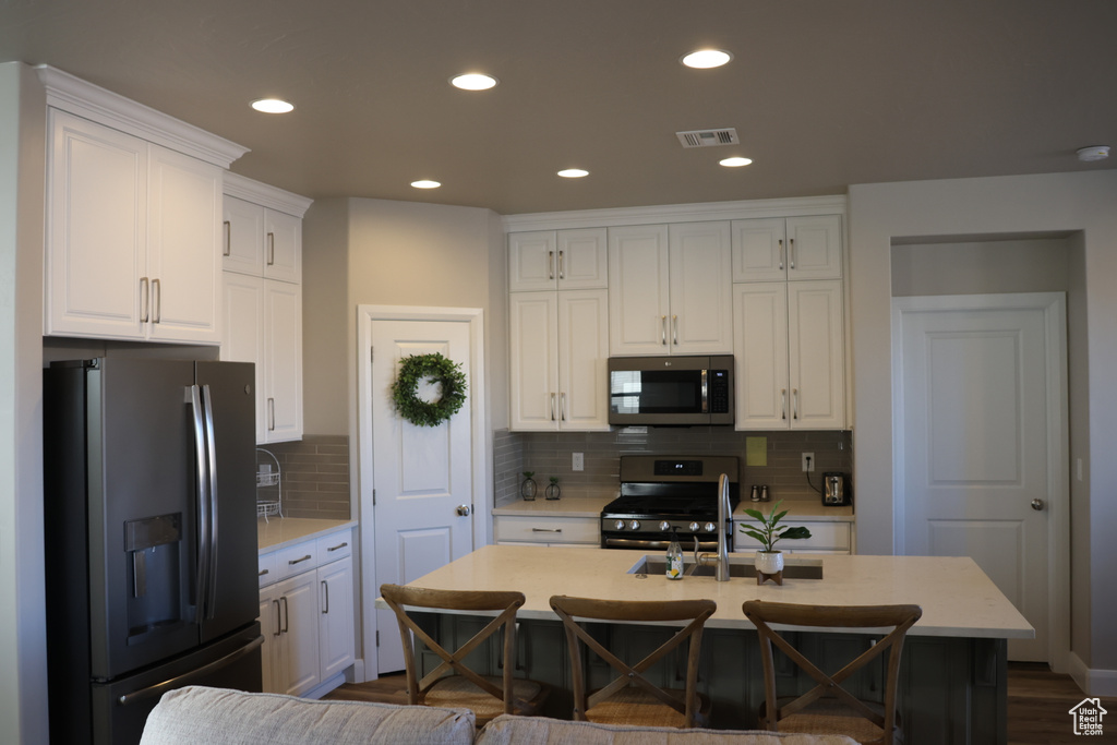 Kitchen with tasteful backsplash, white cabinets, stainless steel appliances, and hardwood / wood-style flooring