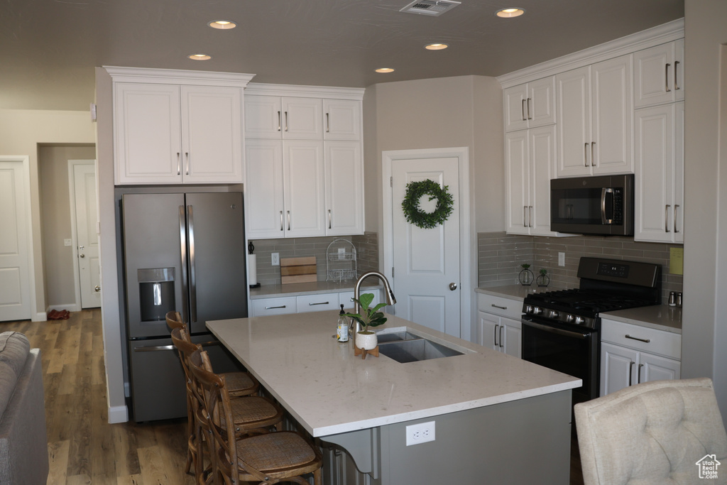 Kitchen featuring a center island with sink, stainless steel appliances, sink, a breakfast bar, and white cabinetry