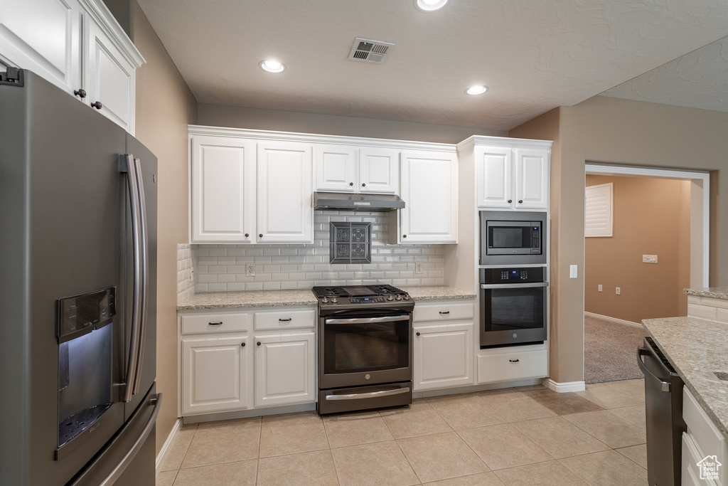 Kitchen with white cabinetry, stainless steel appliances, light tile floors, and tasteful backsplash