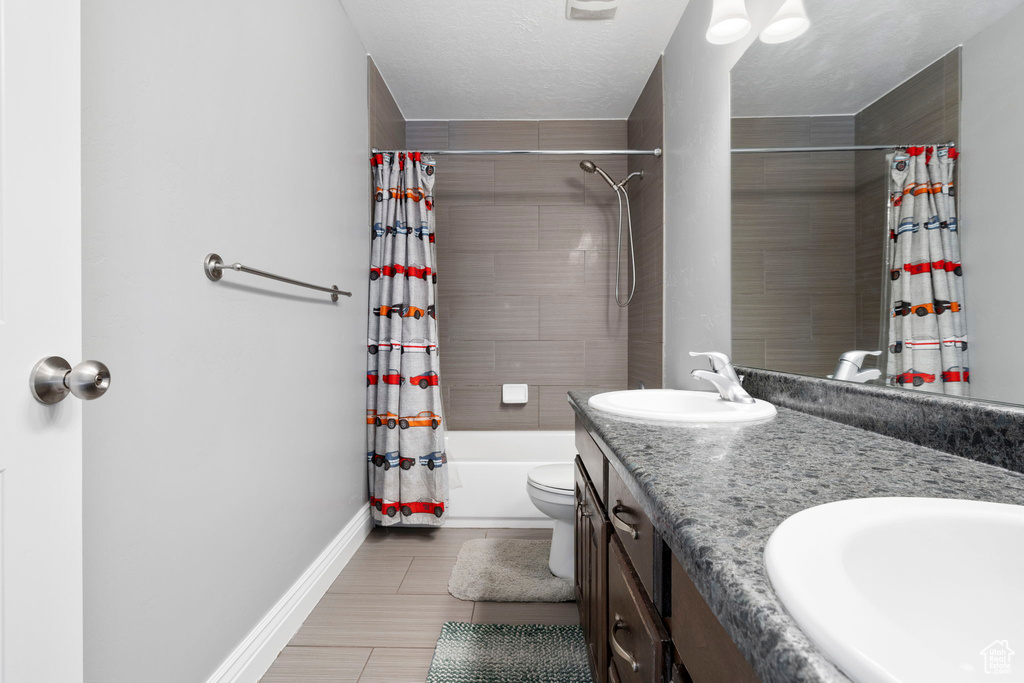 Full bathroom with dual sinks, shower / bath combo, tile flooring, oversized vanity, and toilet
