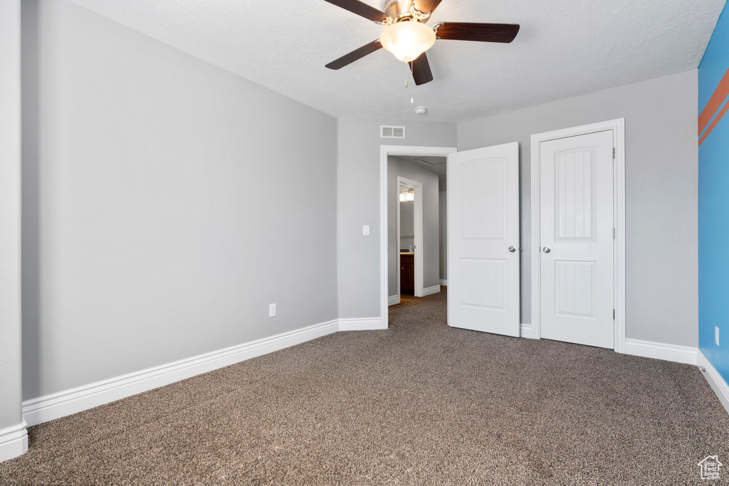 Unfurnished bedroom with a closet, dark carpet, and ceiling fan