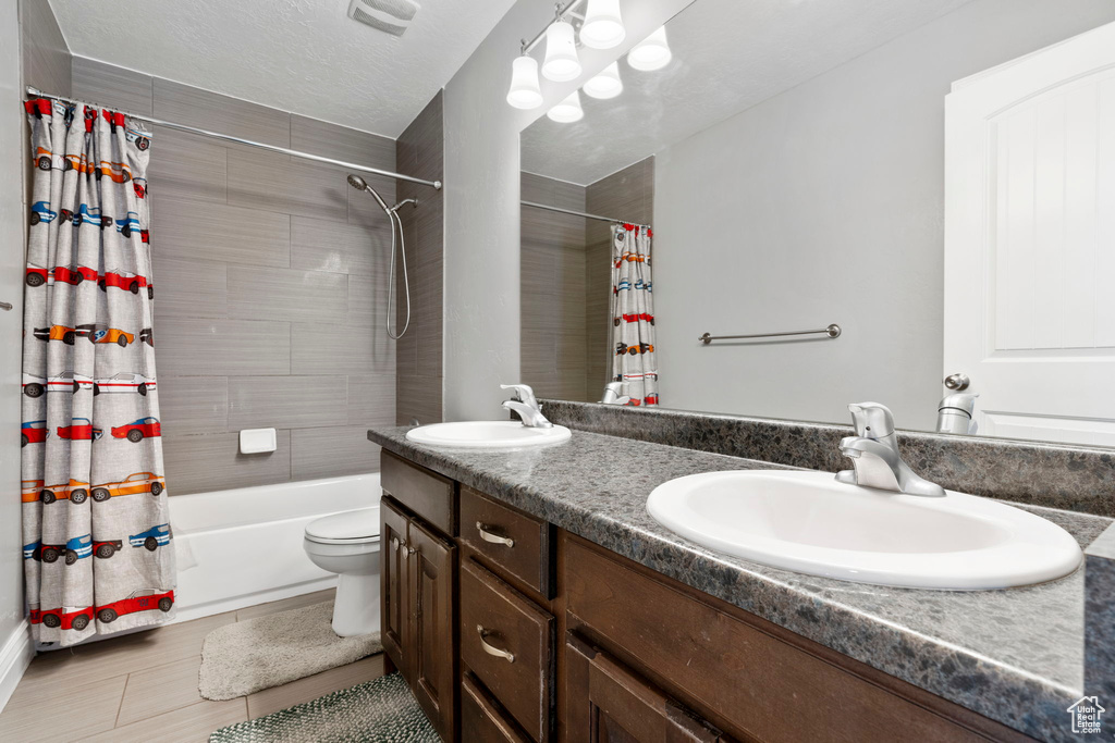 Full bathroom with double sink, tile floors, large vanity, toilet, and shower / bathtub combination with curtain