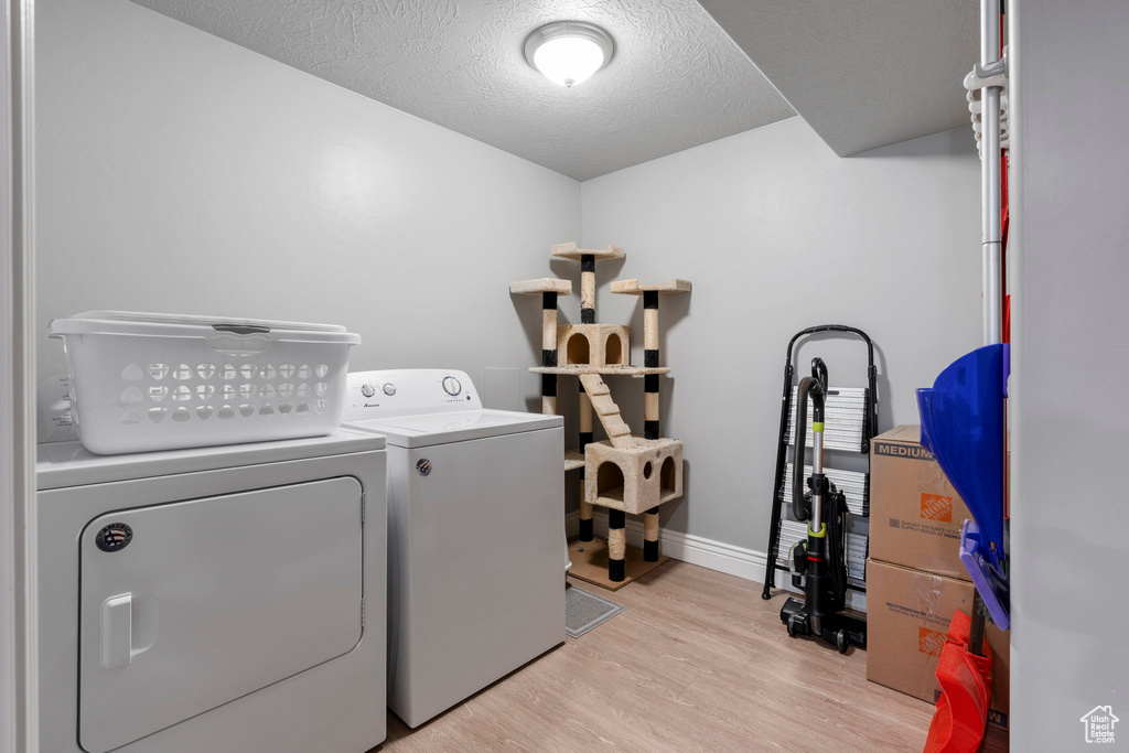 Washroom featuring a textured ceiling, washer and clothes dryer, and light hardwood / wood-style floors