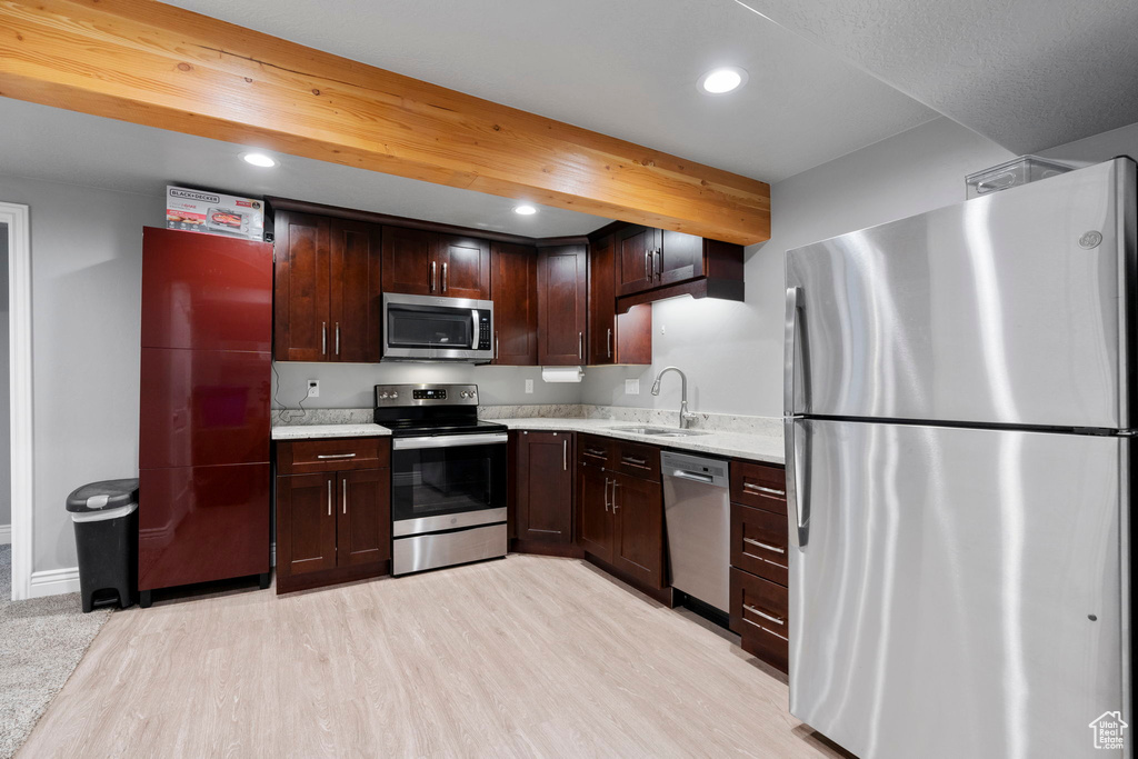 Kitchen with dark brown cabinets, light hardwood / wood-style flooring, sink, appliances with stainless steel finishes, and light stone countertops