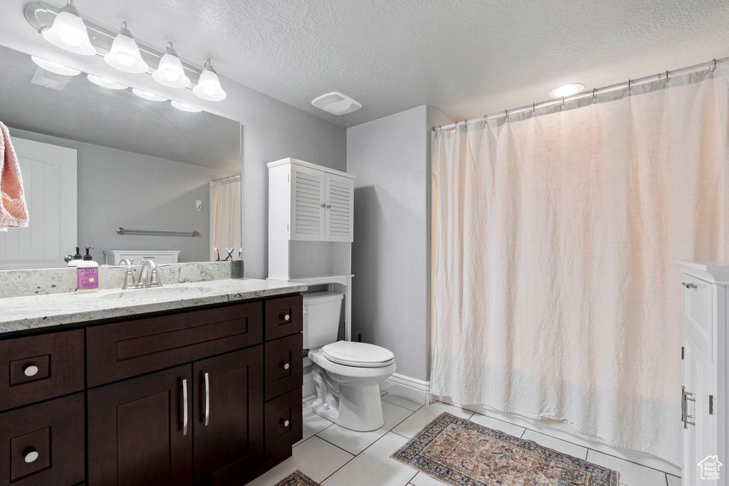 Bathroom featuring a textured ceiling, tile flooring, vanity with extensive cabinet space, and toilet