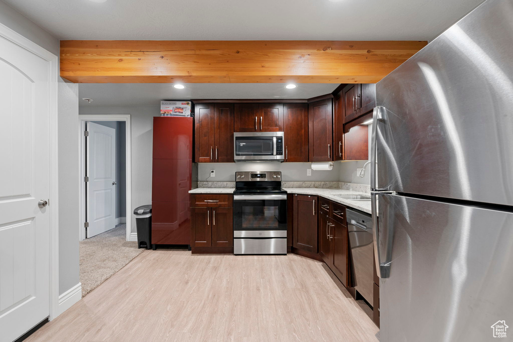 Kitchen featuring appliances with stainless steel finishes, dark brown cabinets, sink, and light hardwood / wood-style floors