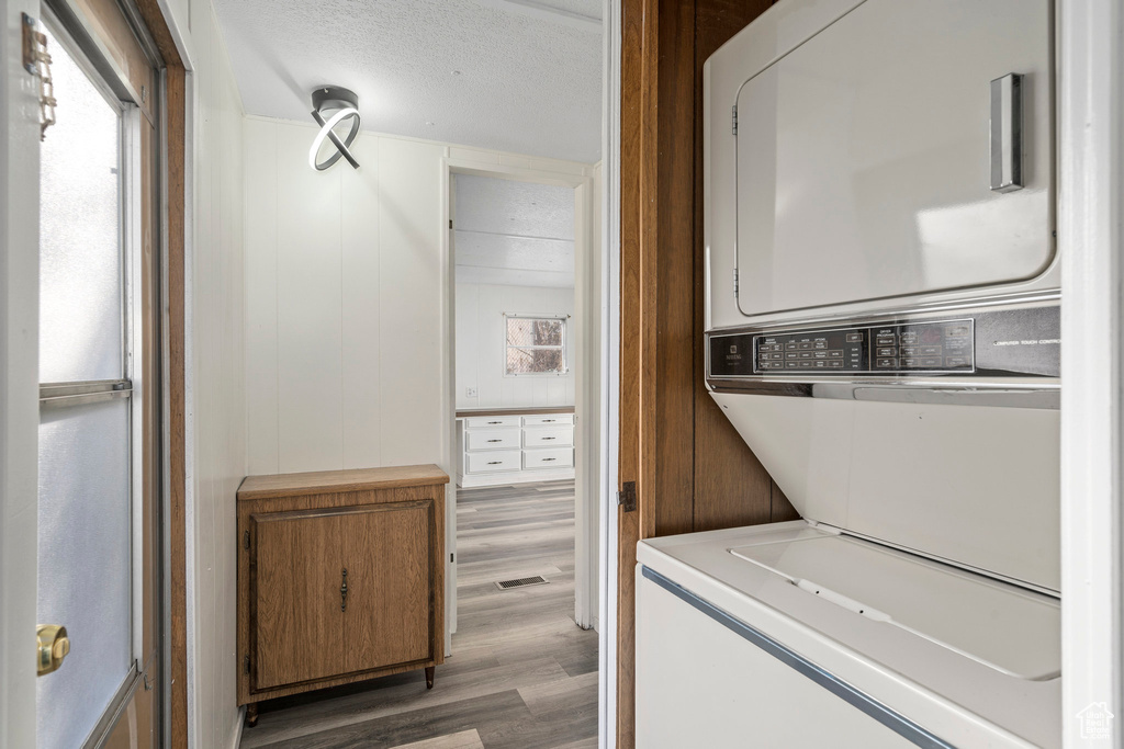 Laundry area with dark wood-type flooring, stacked washer and dryer, and a textured ceiling