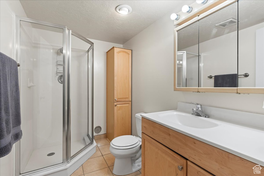 Bathroom featuring a textured ceiling, walk in shower, toilet, tile flooring, and vanity