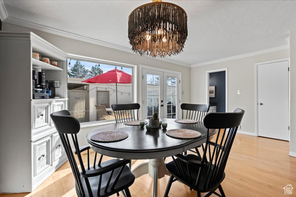 Dining space featuring french doors, ornamental molding, a notable chandelier, and light hardwood / wood-style flooring