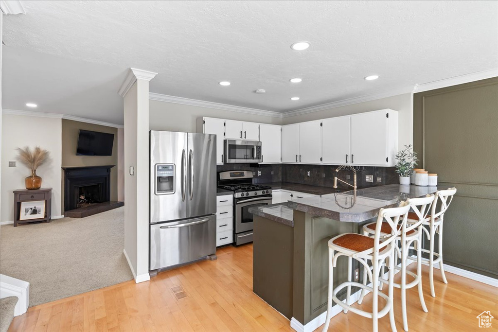 Kitchen featuring light colored carpet, backsplash, white cabinetry, kitchen peninsula, and stainless steel appliances