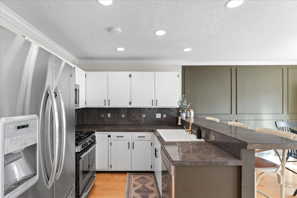Kitchen with white cabinets, appliances with stainless steel finishes, light hardwood / wood-style floors, and backsplash