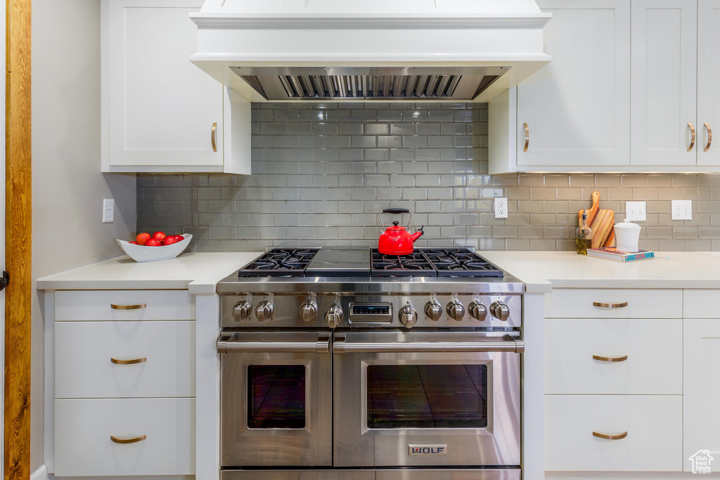 Kitchen with custom range hood, double oven range, backsplash, and white cabinets
