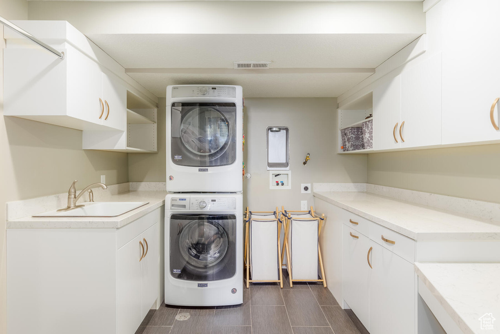 Washroom featuring cabinets, sink, stacked washer and dryer, and dark tile floors