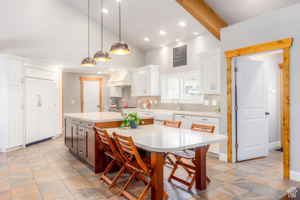 Kitchen featuring white cabinets, backsplash, a breakfast bar area, hanging light fixtures, and a kitchen island with sink