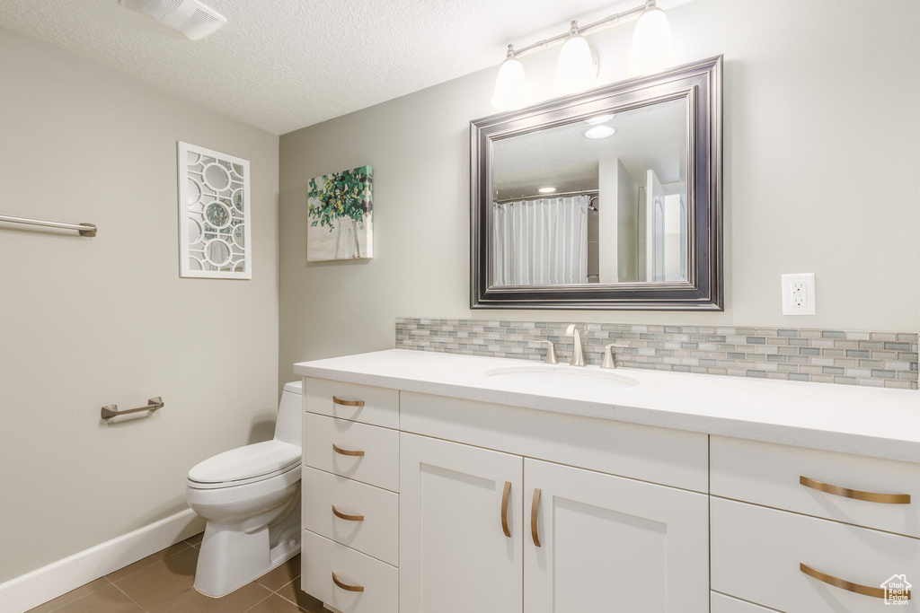 Bathroom featuring vanity, tile flooring, tasteful backsplash, toilet, and a textured ceiling