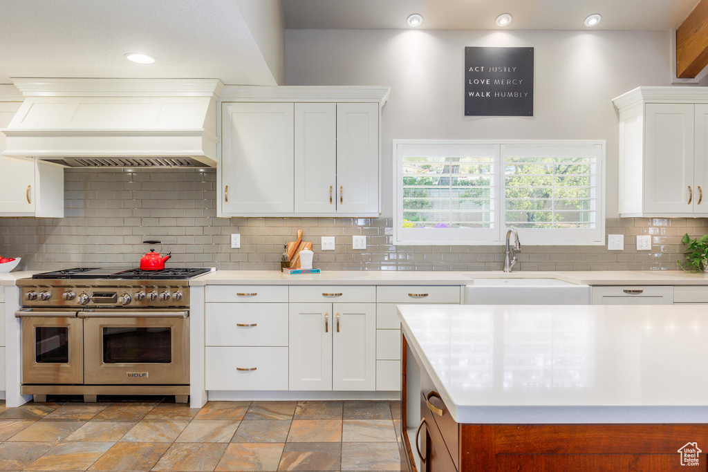 Kitchen featuring range with two ovens, tasteful backsplash, premium range hood, and light tile flooring