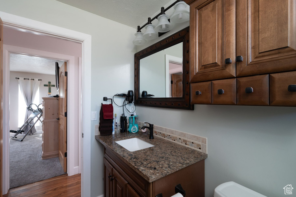 Bathroom featuring a textured ceiling, hardwood / wood-style floors, oversized vanity, and toilet