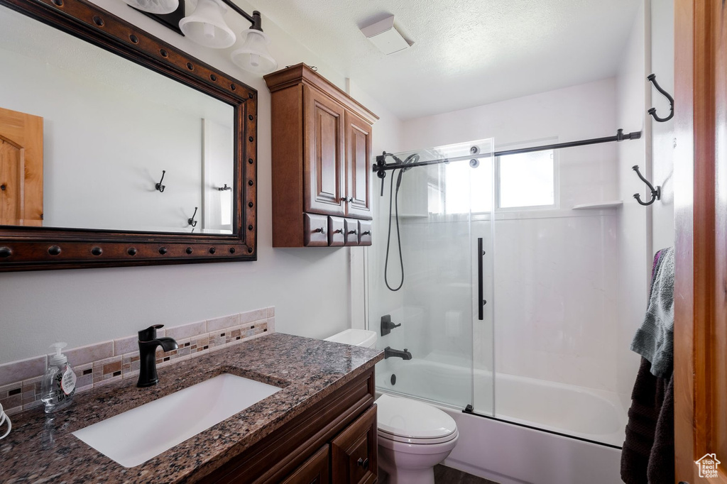 Full bathroom featuring combined bath / shower with glass door, a textured ceiling, vanity with extensive cabinet space, and toilet