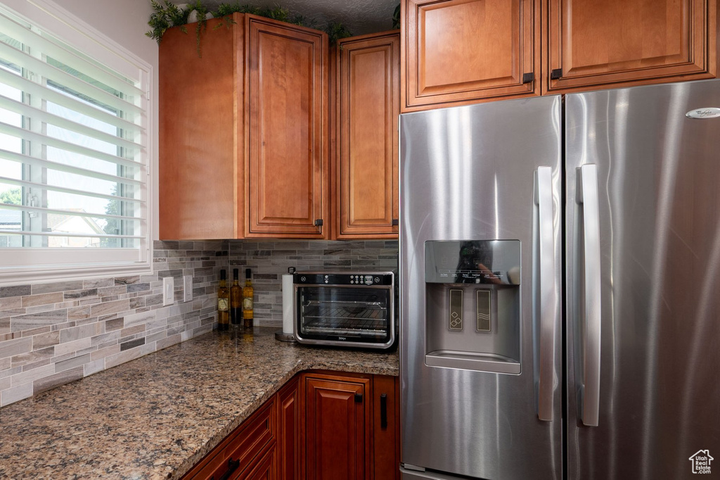 Kitchen featuring backsplash, stainless steel refrigerator with ice dispenser, and light stone counters