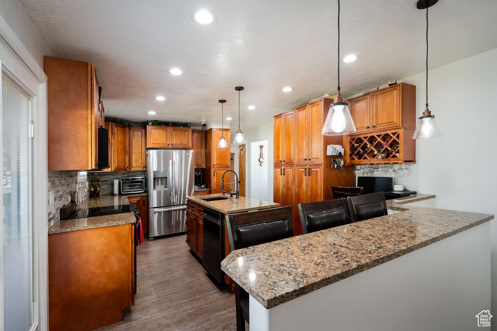 Kitchen with a kitchen island with sink, light stone countertops, dark hardwood / wood-style floors, pendant lighting, and stainless steel fridge