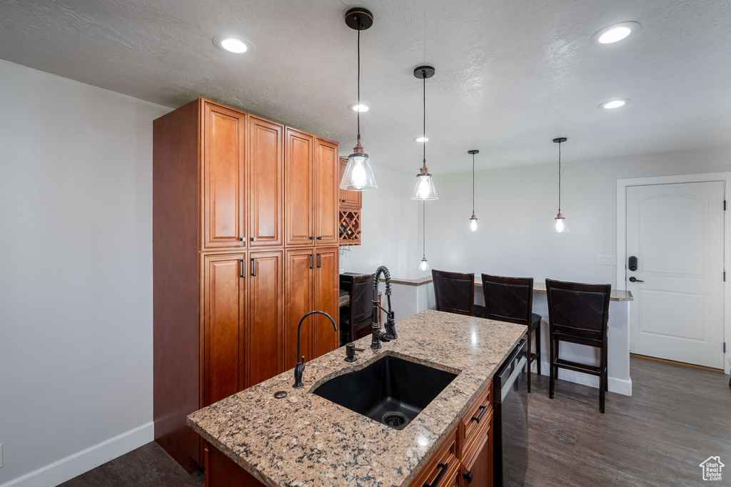 Kitchen with pendant lighting, dishwashing machine, dark hardwood / wood-style floors, light stone countertops, and a center island with sink