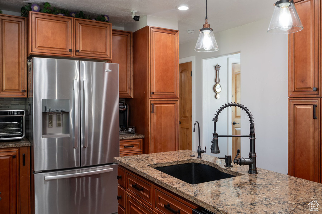 Kitchen featuring backsplash, light stone countertops, sink, hanging light fixtures, and stainless steel fridge
