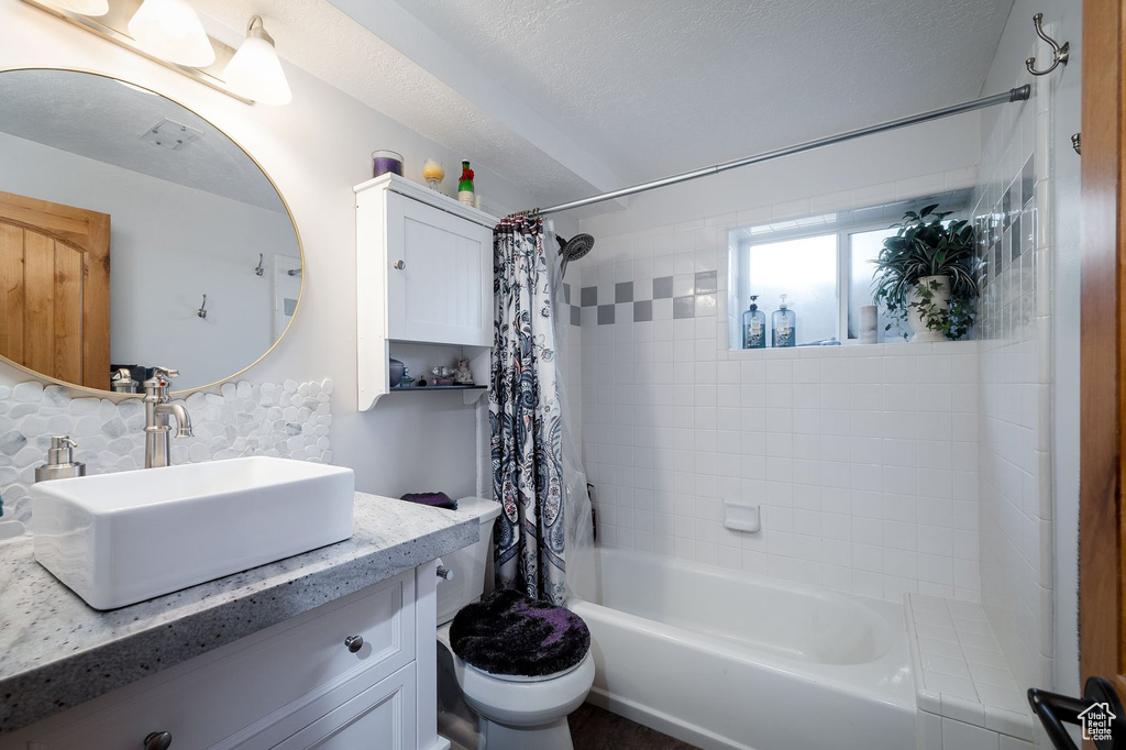 Full bathroom featuring shower / bath combo, vanity, toilet, and a textured ceiling
